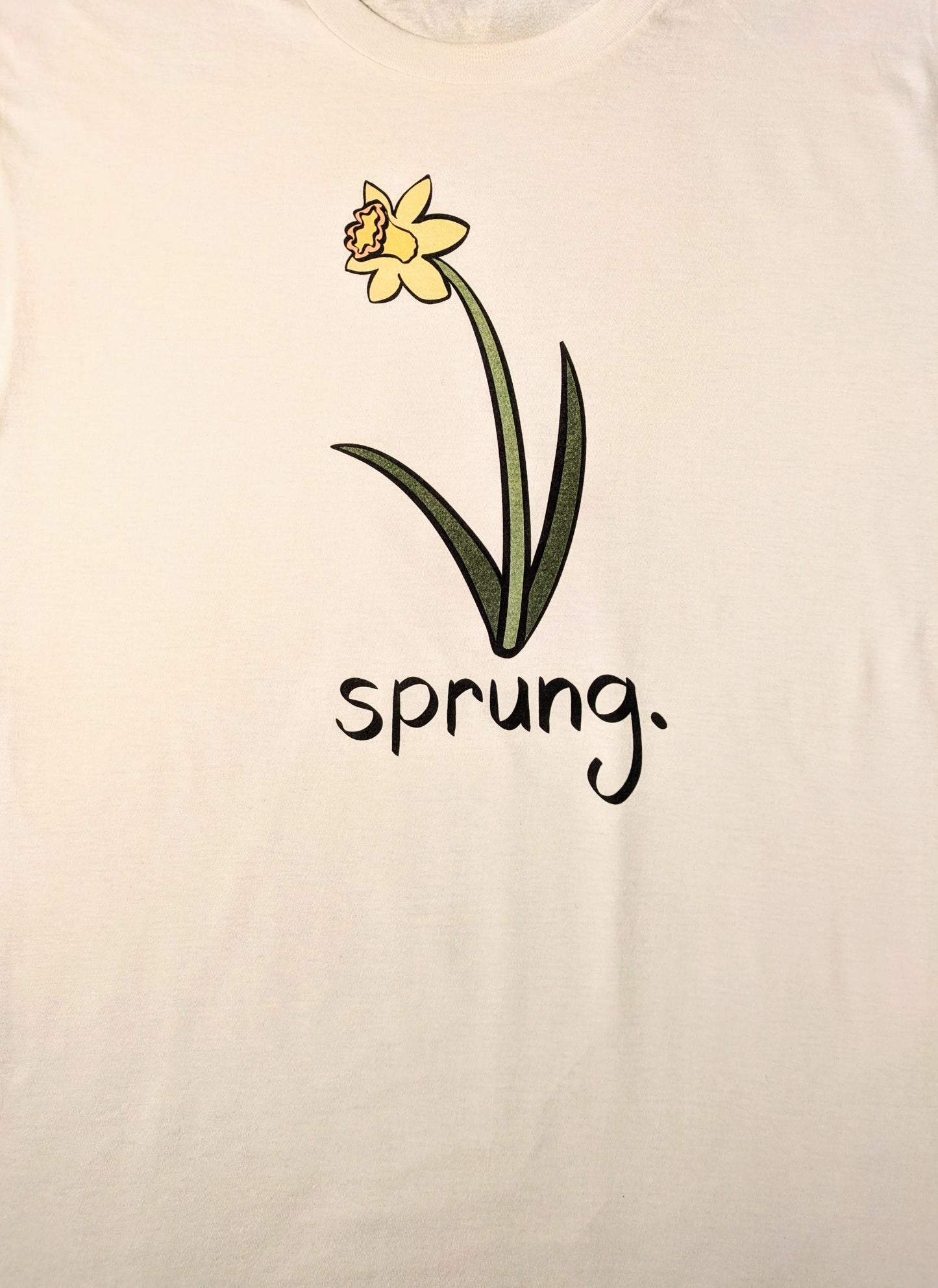 White t-shirt with a daffodil graphic and 'sprung.' text on a white background