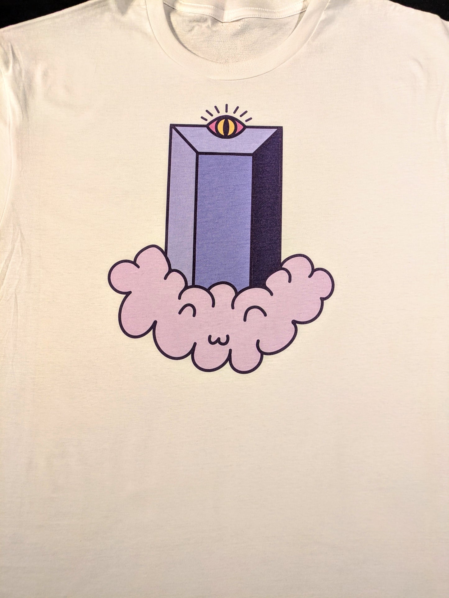 A white tee with a cartoonish version of the Fifth Third Building in Lexington. It has a Radiant eye at the top and is sitting on top of a light purple floating cloud that has a chibi like smiling face