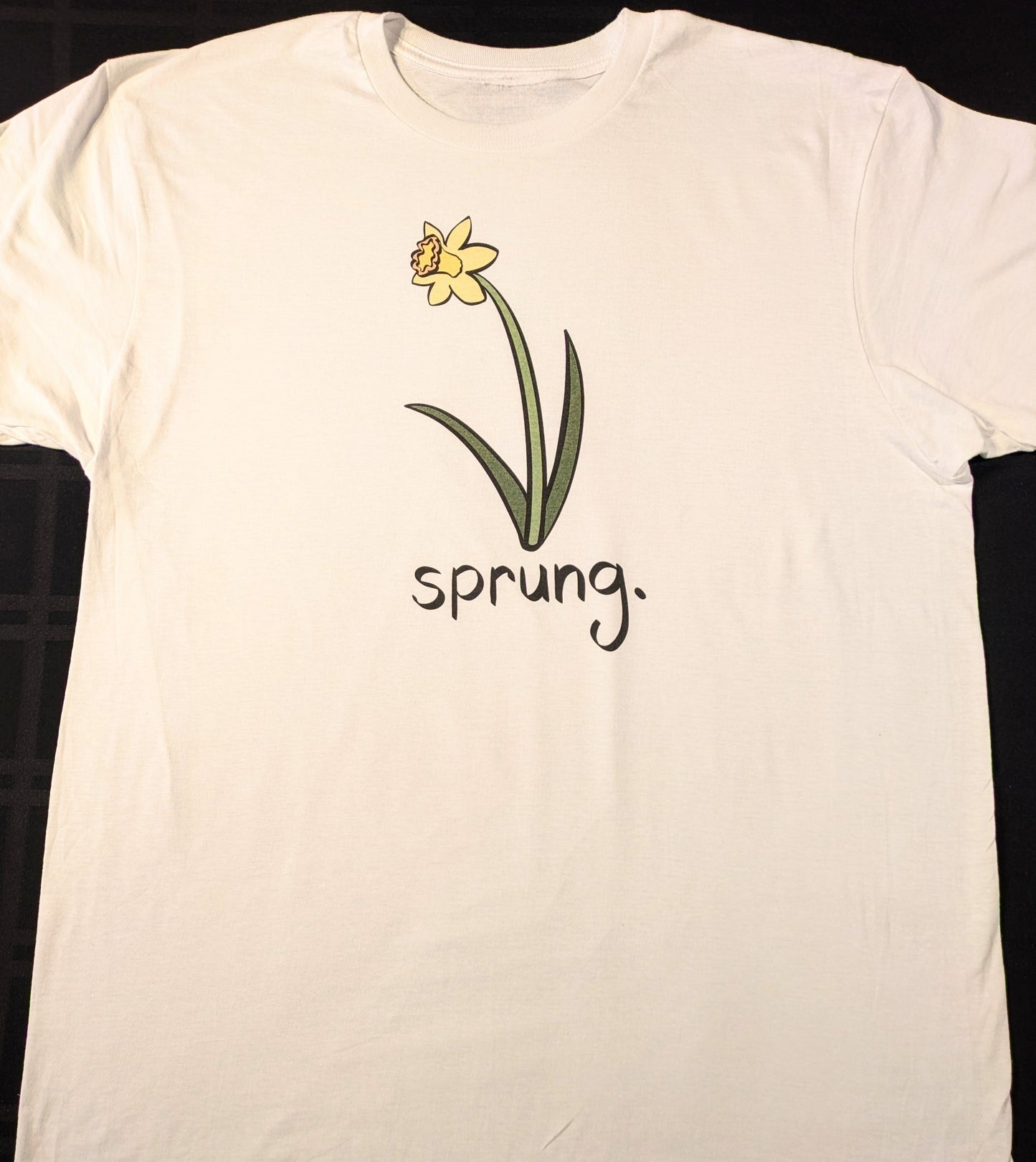 White t-shirt with a yellow daffodil flower graphic and 'sprung.' text on a black background